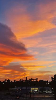 an orange and blue sky at sunset with some clouds in the foreground as cars drive by