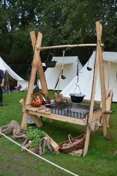 a wooden stand with pots and pans on it in the grass near some tents