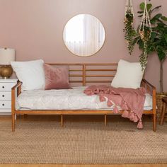 a day bed with pillows and blankets on it in front of a round mirror over a dresser