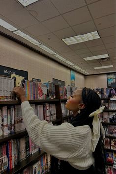 a woman in a library picking up a book from a shelf with several books on it