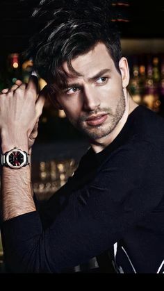 a man with a watch on his wrist posing for a photo in front of a cityscape