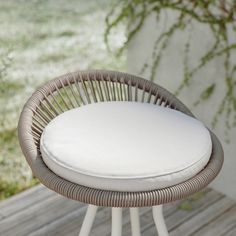 a wicker stool with white cushions on a wooden deck in front of a plant