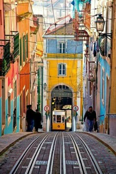 two people are walking down the street in front of an old train track and colorful buildings