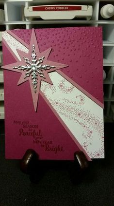 a pink and white christmas card with a snowflake on the front, two pieces of chocolates below it