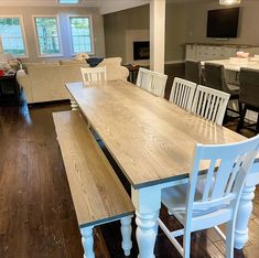 a dining room table and chairs in a living room with hardwood floors, white painted furniture and large windows