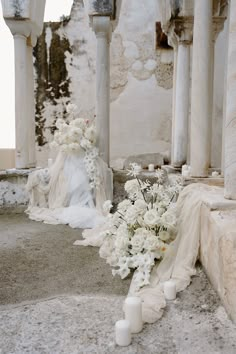 white flowers and candles sit on the ground in front of an old building with columns