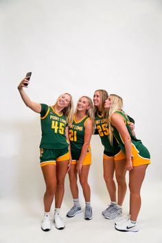 three young women in green and yellow uniforms taking a selfie with a cell phone