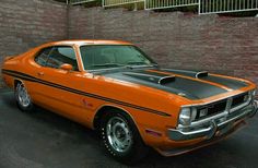 an orange muscle car parked in a parking lot next to a brick wall and fence