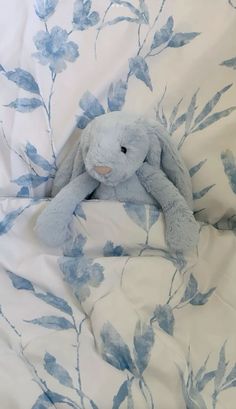 a blue and white stuffed animal sitting on top of a bed covered in sheets with leaves