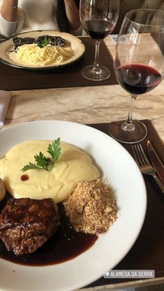 a white plate topped with meat and gravy next to a glass of wine