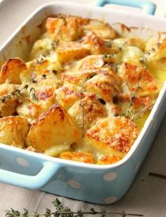 a casserole dish with potatoes and meat in it sitting on a table next to some herbs