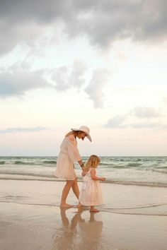 a mother and daughter walking on the beach at sunset with an ocean in the background