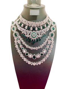 This CZ American Diamond Necklace Set features a multilayer design adorned with green stones. The intricate craftsmanship and sparkling stones make this a stunning addition to any jewelry collection. Enjoy the sophisticated and elegant look of this necklace set at any event or occasion. This jewellery set includes a necklace and matching earrings. Jewellery Care- Keep the jewellery dry, avoid contact with perfumes and water. Dazzling Green Stone Necklaces, Green Diamond Jewelry Sets For Reception, Party Bridal Necklace With Intricate Design In Green, Green Bridal Necklace With Intricate Design For Party, Green Emerald Necklace With Elegant Design, Green Emerald Necklace With Intricate Design, Green Emerald Bridal Necklace With Elegant Design, Elegant Green Emerald Necklace For Wedding, Elegant Green Emerald Bridal Necklace