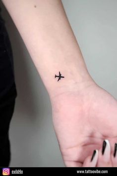 an airplane tattoo on the wrist is shown in black ink, and it appears to be flying