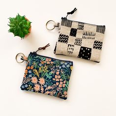 two zippered pouches sitting next to each other on a white surface with a plant in the background