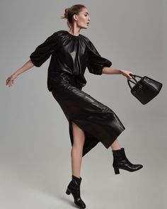 a woman in a black dress and boots is holding a handbag with her right leg