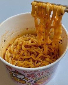 noodles being lifted from a cup with chopsticks in it to be eaten by someone