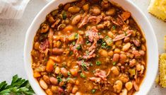 a white bowl filled with beans, ham and cornbreads on top of a table