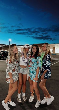 four girls are standing in a parking lot at night with their arms around each other