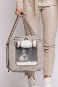 a woman holding a gray and white bag with a dog in it