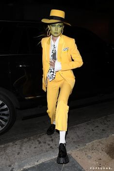 a man in a yellow suit and hat is walking down the street with his hand on his hip