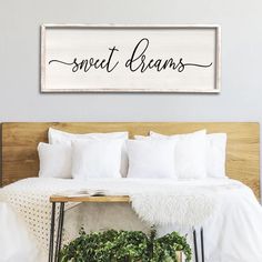 a bed with white sheets and pillows in front of a wooden sign that says sweet dreams