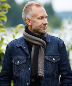 a man wearing a scarf and jacket looks off into the distance with trees in the background