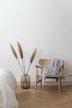 a white room with a chair, vase and plant on the floor next to it