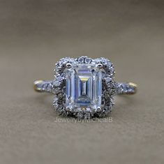 an emerald cut diamond surrounded by diamonds on top of a gold and silver band ring