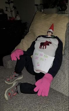 an elf is sitting on the couch with his feet up and wearing pink gloves while holding a t - shirt that says, you may fly like you