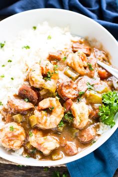 a white bowl filled with shrimp and rice on top of a wooden table next to a blue napkin