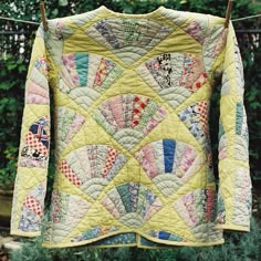 an old quilt hanging on a clothesline in front of some trees and bushes,