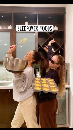 two young women are baking cookies together in the kitchen, one is holding a pan with doughnuts on it