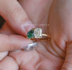 a woman's hand holding an engagement ring with a green and white diamond in it