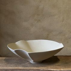 a large white bowl sitting on top of a wooden table next to a cement wall