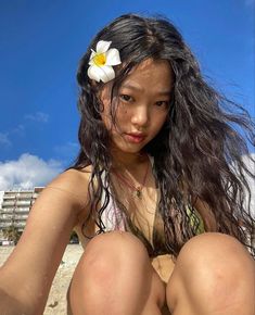 a woman sitting on the beach with a flower in her hair and wearing a bathing suit