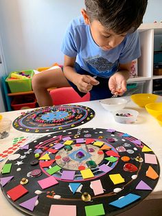 a boy sitting at a table making art with colored paper and magnets on it