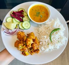 a white plate topped with rice and veggies next to a bowl of soup