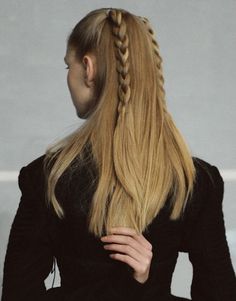 a woman with long blonde hair wearing a black dress and braiding her hair into a pony tail