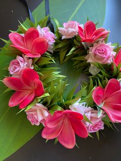 a wreath made out of pink and white flowers on top of a green leafy surface