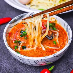 a bowl of soup with chopsticks sticking out of it and noodles in the background