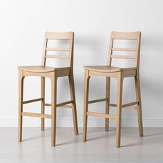 two wooden stools sitting next to each other in front of a white wall and floor