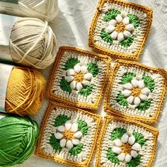 four crocheted squares with white flowers on them and balls of yarn in the background