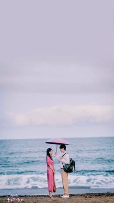 two people standing under an umbrella on the beach