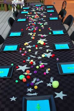 a long table is decorated with black and blue place mats, neon colored confetti, and stars