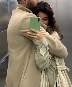 a man and woman hugging each other while looking at their cell phones in an elevator