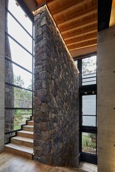 the interior of a modern house with stone walls and wooden steps leading up to an open floor plan