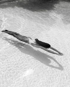 a man floating in the water on top of a swimming pool next to another person