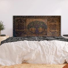 a bed with white sheets and a tree on the wall above it, in a bedroom