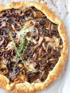 a mushroom and cheese pizza with a sprig of thyle on top, sitting on parchment paper